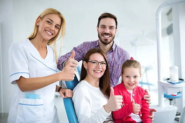 A satisfied family giving a thumbs up with the hygienist at the dentist office, suggesting a successful dental visit.